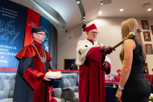 The Rector, wearing ceremonial attire, conducts the matriculation of a female student standing in front of the stage. A representative of the university authorities wearing an academic gown stands beside them.