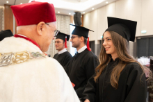 A person in a black academic gown and mortarboard stands in front of a person in ceremonial red-and-white academic attire during the diploma presentation ceremony.