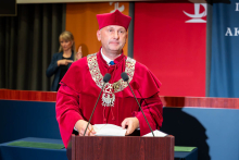 A representative of the university authorities wearing a red academic gown speaks at the lectern during the inauguration of the academic year. A Polish Sign Language interpreter is visible in the background.