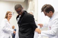 A university representative helps a male student put on a white coat during the ceremony.