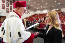 The Rector, wearing ceremonial attire, presents a document to a female student and shakes her hand during the academic year inauguration ceremony.