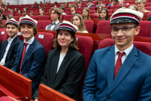Four students wearing student caps sit in the auditorium during the academic year inauguration ceremony.