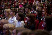 A full auditorium with participants seated in rows of red seats and watching the event.
