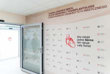 A wall featuring the logos of the Medical University of Warsaw and the clinic serves as a photo backdrop. A glass entrance is located next to it. The wall bears the inscription: “Whoever saves one Heart saves the whole World