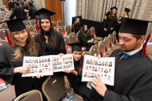 People in academic gowns and mortarboards before the graduation ceremony, displaying open photo albums.