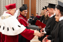 People in ceremonial academic robes shake hands with participants in black academic gowns and mortarboards during the diploma presentation ceremony.