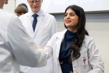A female student wearing a white coat shakes hands with a university representative, who is also wearing a white coat.