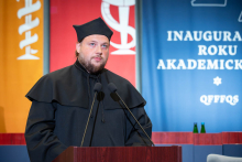 A representative of the academic community speaks at the lectern against the backdrop of the academic year inauguration decorations.