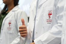 Two people wearing white coats are standing next to each other. One of them is giving a thumbs-up gesture. The logo and the words “Faculty of Medicine, Medical University of Warsaw” are visible on the coat pockets.