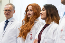 Four people wearing white coats are standing next to each other during the ceremony. The logo and the words “Faculty of Medicine, Medical University of Warsaw” are visible on their coats.