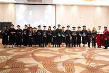 A group of people in black academic gowns and mortarboards pose for a group photo, displaying diplomas and awards; people in ceremonial academic robes stand on either side.