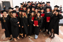 A large group of people in black academic gowns and mortarboards pose for a group photo after the ceremony; some are holding red diploma folders.