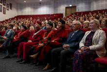 Przedstawiciele uczelni w ceremonialnych togach oraz pozostali goście siedzą w pierwszym rzędzie wypełnionego audytorium.