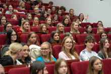 Widok na audytorium wypełnione studentami siedzącymi na czerwonych krzesłach w sali wykładowej.