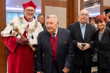 Four people pose for a photo after the academic ceremony; one is wearing red-and-white academic robes and holding a mace.