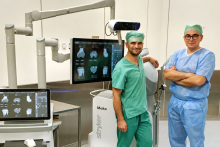 Two people are standing next to a robotic system. The screens display models and parameters related to knee surgery planning.