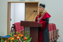 A person in an academic gown and mortarboard speaks at the lectern during the ceremony.