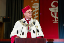 The Rector, wearing ceremonial academic attire, delivers a speech at the lectern.