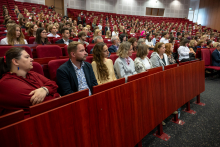 Licznie zgromadzeni uczestnicy siedzą w czerwonych fotelach audytorium i obserwują przebieg uroczystości.