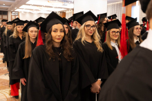 A large group of people in black academic gowns and mortarboards stand in line in the hall during an academic ceremony.