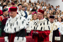 Guests wearing academic gowns sit in the auditorium and take part in the ceremony.