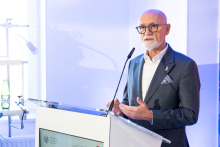 Dr Tomasz Maciejewski speaks at a lectern during an event at the Department of Cardiac, Thoracic Surgery and Transplantology. Part of the clinical room and medical equipment can be seen in the frame.