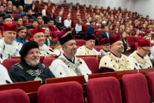 Guests wearing academic gowns sit in the auditorium and take part in the ceremony.