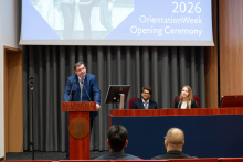The Vice-Dean of the Faculty of Medicine and Dentistry speaks at the podium during the opening of Orientation Week 2026. Two people are seated at the head table.