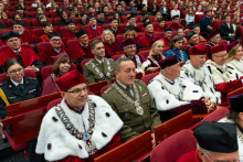 Guests wearing academic gowns sit in the auditorium and take part in the ceremony.