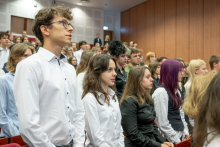 Grupa uczestników stoi wśród rzędów czerwonych foteli podczas uroczystości w audytorium.