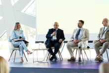Cztery osoby uczestniczą w panelu dyskusyjnym. Jedna osoba mówi do mikrofonu, a pozostałe siedzą obok na scenie.