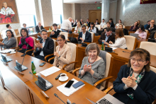 Uczestnicy uroczystości siedzą przy stołach w sali obrad, część osób bije brawo.