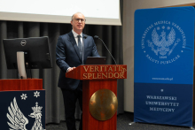 Jedna osoba przemawia przy mównicy z dwoma mikrofonami podczas Kongresu Pharmacovigilance Polska 2026. Obok stoi baner Warszawskiego Uniwersytetu Medycznego.