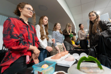 Grupa osób stoi przy stoisku jednego z kół naukowych. Na stole znajdują się modele anatomiczne oraz materiały wykorzystywane do ćwiczeń praktycznych.