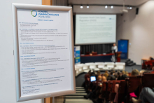 Jedna osoba przemawia przy mównicy z dwoma mikrofonami podczas Kongresu Pharmacovigilance Polska 2026. Obok stoi baner Warszawskiego Uniwersytetu Medycznego.