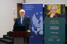 Rektor przy mównicy z laptopem i mikrofonami. W tle widoczny jest ekran prezentacji z napisem „Everything is Chemistry” oraz portretem prelegenta wydarzenia.