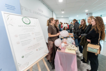Osoby rozmawiają przy stoisku Studenckiego Koła Naukowego Ginekologia. Na stole znajdują się model miednicy, materiały informacyjne i różowe balony.