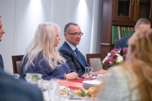 Uczestnicy spotkania siedzą przy stole konferencyjnym. Jedna osoba zabiera głos, a pozostali słuchają.