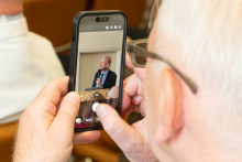 Osoba siedząca na sali nagrywa telefonem wystąpienie prowadzącego wykład.