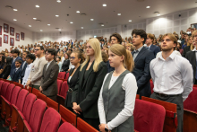 Uczestnicy stoją między rzędami czerwonych foteli w auli i składają przyrzeczenie.