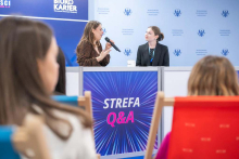 Dwie prelegentki siedzące przy stoliku z mikrofonem podczas panelu dyskusyjnego w „Strefie Q&A” na tle niebieskiej ścianki Warszawskiego Uniwersytetu Medycznego.