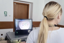 Młoda kobieta wykonuje ćwiczenie na symulatorze chirurgicznym. Na monitorze widoczna jest grafika wykorzystywana podczas treningu koordynacji ruchowej.