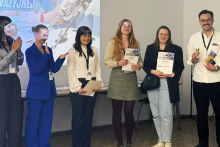 Cztery osoby z dyplomami podczas ceremonii zakończenia konkursu. Obok stoją organizatorzy wydarzenia.