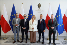 Pięć osób pozuje do wspólnego zdjęcia w budynku Senatu Rzeczypospolitej Polskiej. W tle widoczne są flagi Polski i Unii Europejskiej oraz godło państwowe z napisem „Senat Rzeczypospolitej Polskiej”