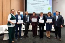 Seven people posing for a group photo during the Pharmacovigilance Polska 2026 Congress. Some of them are holding framed certificates.