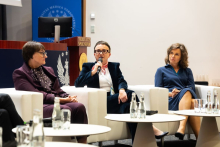 Three participants in an expert debate seated in white armchairs. The person in the middle is speaking into a microphone.