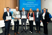 Six participants of the Pharmacovigilance Polska 2026 Congress posing for a group photo. Four of them are holding framed certificates.