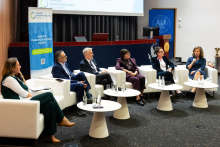 Six participants in an expert debate during the Pharmacovigilance Polska 2026 Congress. The participants are seated in white armchairs in front of a screen displaying the debate topic on adverse reactions and treatment.