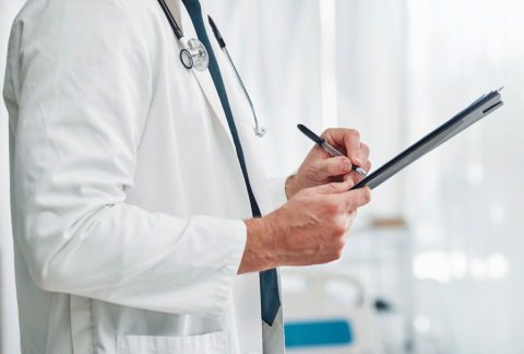  A man in a white doctor's coat, with a stethoscope slung over his shoulders. In his hands he holds a record and a pen, taking notes