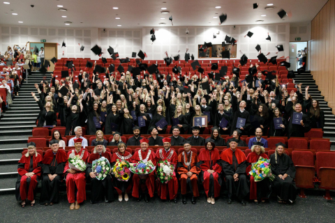 Lecture hall. In the front rows sit teachers in academic togas. In the back stand graduates in student togas - they throw their birettas up in the air.